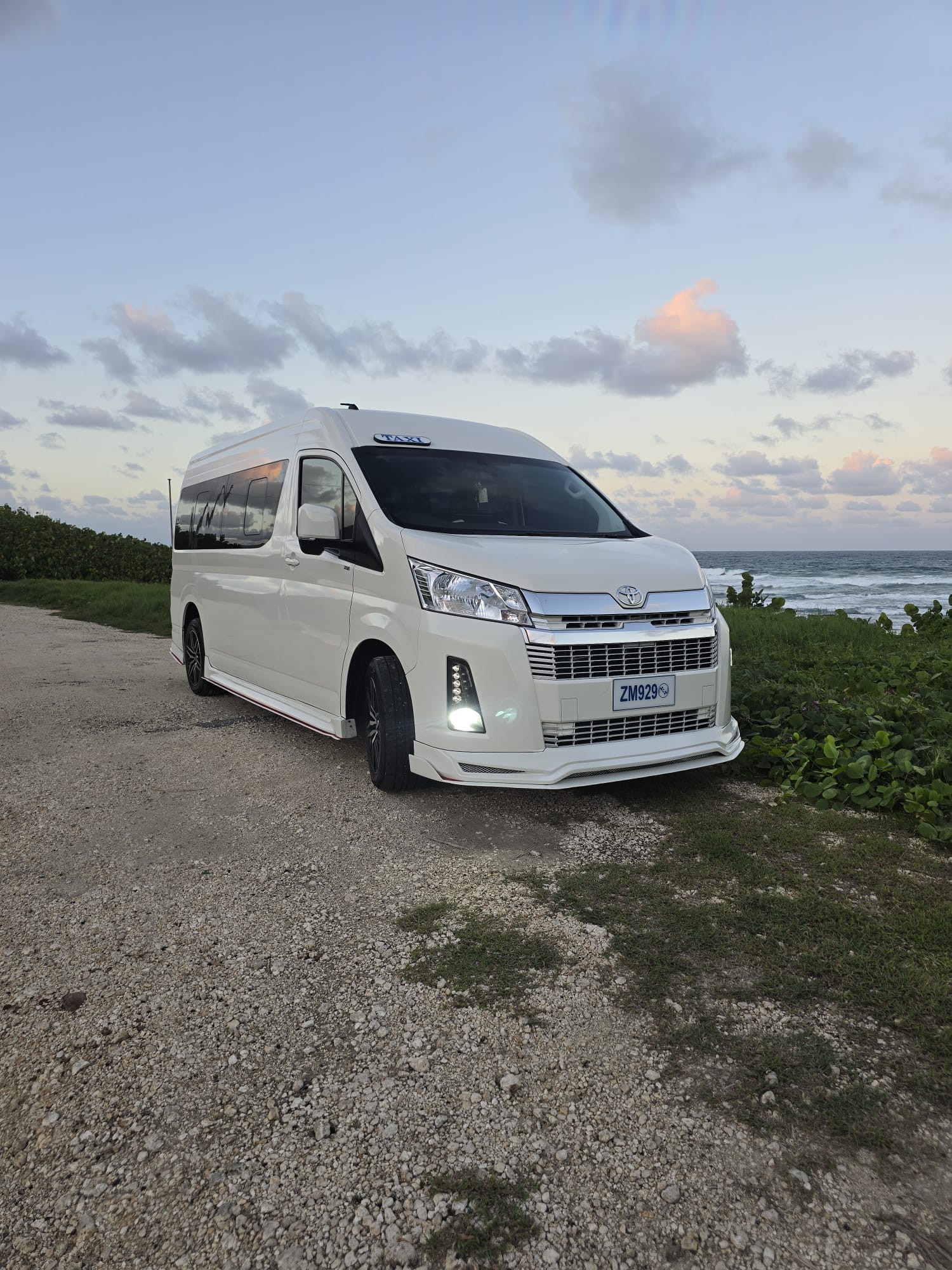 White Unique Chauffeurs van on a Barbados coastal road at sunset
